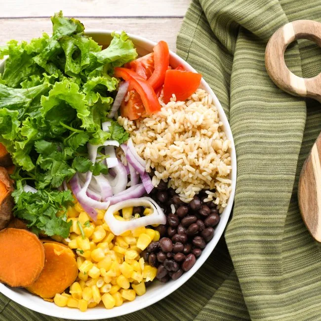 Bol de légumes frais, riz et haricots sur une table en bois
